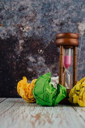 waiting and brainstorming concept, crumpled paper and hourglass on wooden deskの写真素材