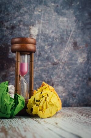 waiting and brainstorming concept, crumpled paper and hourglass on wooden deskの写真素材
