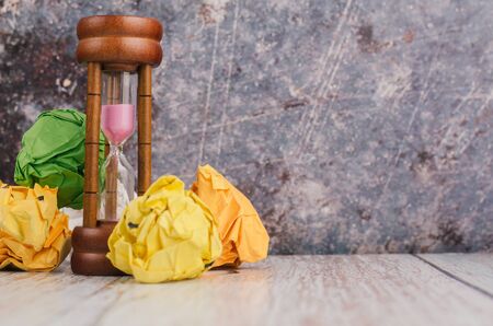 waiting and brainstorming concept, crumpled paper and hourglass on wooden deskの写真素材