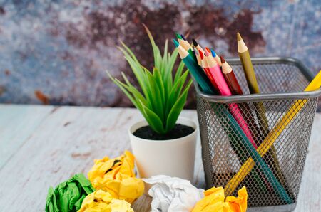 Back to school and offices stationary concept, stack of colored pens marker In a metal case, crumple paper and artificial plant on wooden deskの写真素材