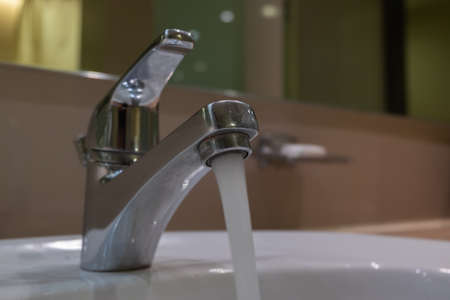 chrome faucet with flowing water in the bathroom. selective focus shotの写真素材