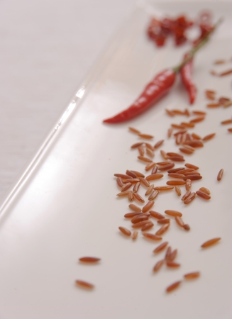 Selective focus on grains of brown rice on white plate with red chilliの写真素材