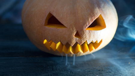 Crazy pumpkin monster on Halloween looks through the smoke. Close - up of scary orange pumpkin faceの写真素材