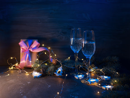 Celebrate Christmas, two glasses of sparkling champagne at night on a table lit with garlands and colored lightsの写真素材
