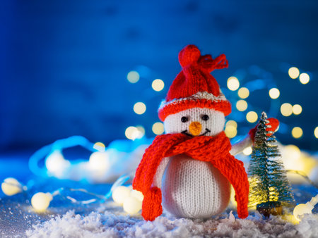 Christmas card with a knitted snowman at the Christmas tree. Fake snow, blue backgroundの写真素材