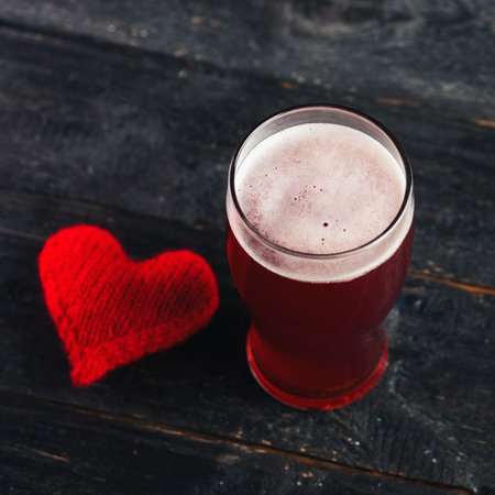 A glass of cold red ale beer on the table with a red heart. The concept of a surprise for a man on Valentine's dayの写真素材