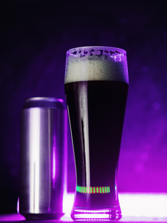 A glass of craft dark beer porter, stout. Neon glowing background, aluminum beer canの写真素材