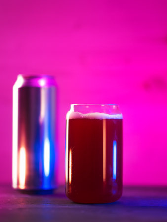 Creative glass in the shape of a beer can. Craft Red fruit beer on a bright neon background,...