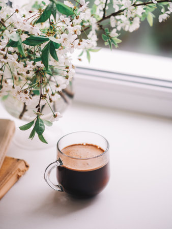 Spring still life on the window, a blooming bouquet of white cherry branches. The concept of Easter or breakfast. Espresso coffee in a glass cupの写真素材