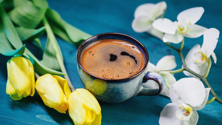 A cup of hot coffee on a blue table and a bouquet of flowers, yellow tulips and a white orchidの写真素材