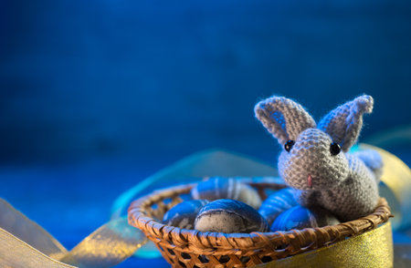 Easter concept. A toy Easter bunny and painted eggs in a wicker basket. Blue backgroundの写真素材