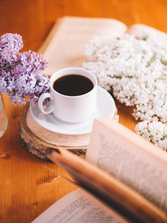 A white cup of coffee on a wooden table. Blooming branches of white lilac, old booksの写真素材