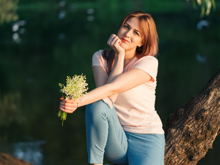 Lovely young woman with a bouquet of flowers on the river Bank on a warm summer eveningの写真素材
