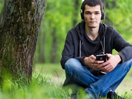 Portrait of a young man sitting in the Park on the grass and listening to music with headphonesの写真素材