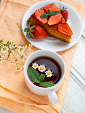 very tasty carrot cake decorated with strawberries on a white table and a Cup of fragrant flower teaの写真素材