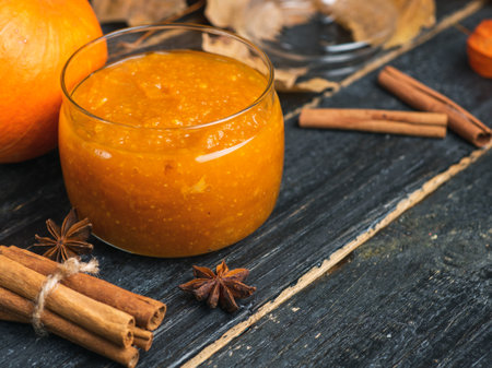 Pumpkin jam in a jar on a wooden background with autumn leaves and cinnamon sticksの写真素材