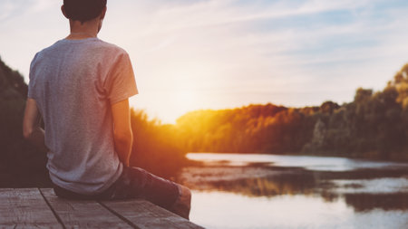 One guy sits on a wooden bridge by the river and admires the sunset and nature in the summerの写真素材
