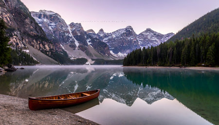 Stunning mountain reflection in a still glacial lake with a rustic wooden canoe resting on the pebbled shore.の素材