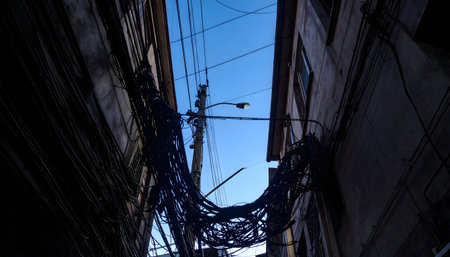 Urban chaos and complexity captured by looking up a tight alley, focusing on the dense, dark silhouette of electrical and telecommunication wires.の素材