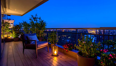 Luxurious, modern high-rise balcony at twilight with a deep blue sky, featuring comfortable seating, potted plants, and a glowing candle lantern.の素材