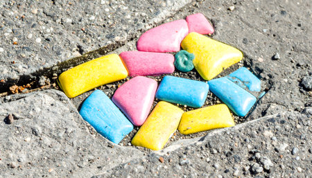 Shallow depth of field macro image of bright, multi-colored steppingstones or recycled plastic pieces on a rough, dark ground.の素材