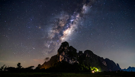 A vertical, wide-angle photograph of the Milky Way galaxy arching over a dark, silhouetted karst mountain landscape on a clear night.の素材