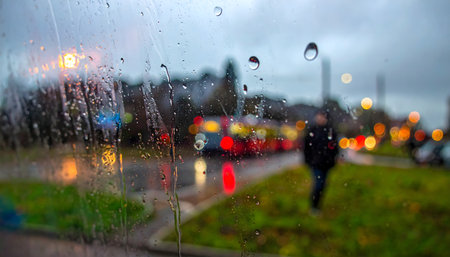 Abstract and atmospheric photograph taken from inside a moving tram or bus on a rainy street at twilight with bokeh lightsの素材