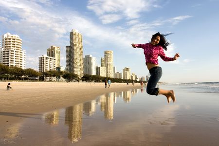 Young adult woman jumping in front of her beach apartment