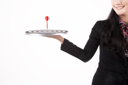 Businesswoman smiling while holding a dartboard with bulls-eye isolated on whiteの写真素材