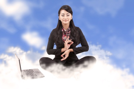 Business woman with laptop meditating sitting on cloudsの写真素材