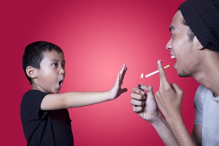 Boy gives warning to smoker shot in studio isolated on redの写真素材