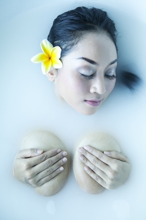 Attractive naked woman enjoys a bath with milk and frangipani petalsの写真素材