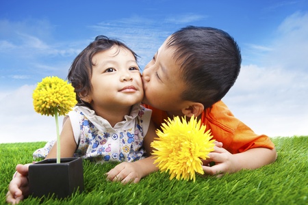 Attractive boy kissing his sister on the green grass with flowersの写真素材