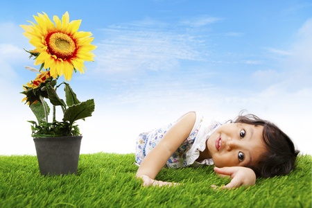 Cute asian girl laying on the grass shot with sunflower in springの写真素材