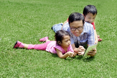 Happy family: Young father with his kids playing digital tablet outdoorの写真素材