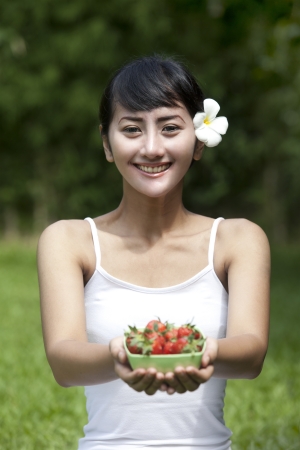 Beautiful Asian woman offering a bowl of strawberryの写真素材