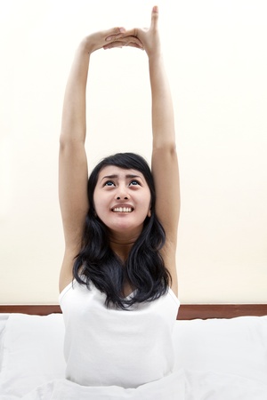 Young asian woman wake-up on the bed and stretch her handの写真素材