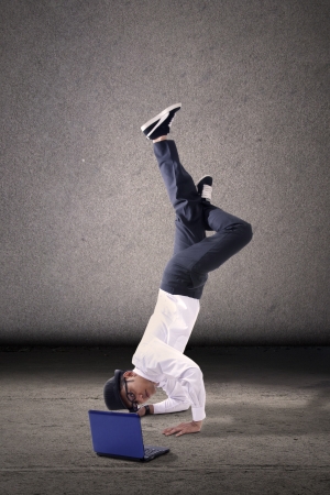 Young asian businessman breakdancing with laptop. shot over grey backgroundの写真素材