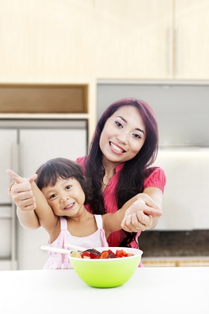 Happy mother and daughter with fruit salad showing thumbs-up. shot in the kitchen の写真素材