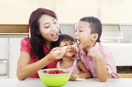Mother and children eating healthy snack - fruit salad. Shot in the kitchenの写真素材