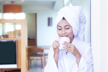 Asian woman wearing bathrobe enjoying cup of coffee at hotel roomの写真素材