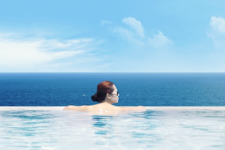 Young asian woman in the swimming pool near the ocean enjoying the ocean viewの写真素材