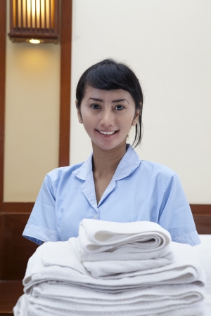 Smiling young cleaning lady holding towels in a hotel room の写真素材