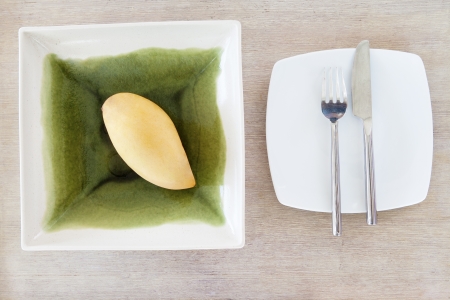 Closeup of yellow mango on a ceramics bowl with fork and saw on plate
