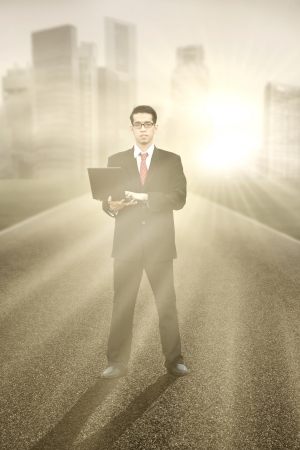 Businessman standing on roadway and using laptop computer to workの写真素材