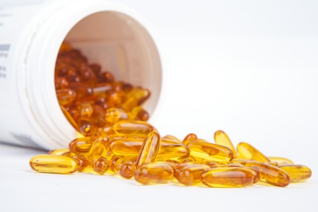Capsules of fish oil spilled out open container  Shot in studio isolated on white