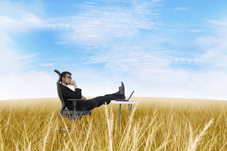 Thoughtful businessman with laptop computer on the fieldの写真素材