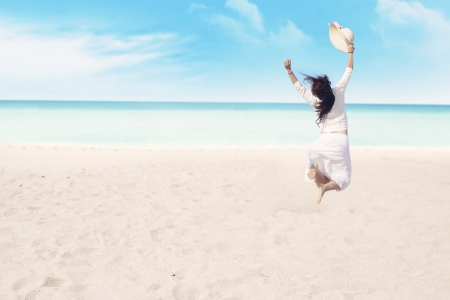Happy carefree woman jumping on beach celebrating her freedomの写真素材