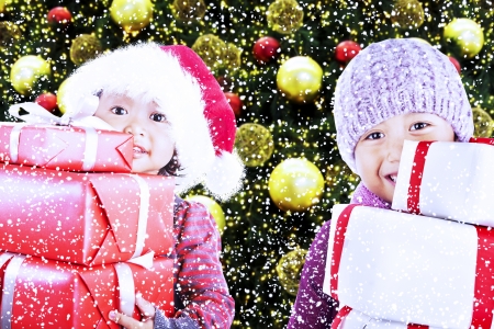 Children bring christmas gifts under the tree while snowing