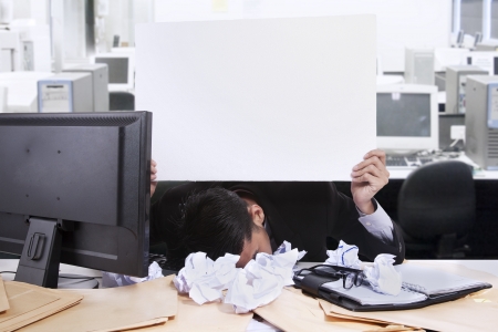 Young businessman with his face down while holding a white copyspace at his officeの写真素材
